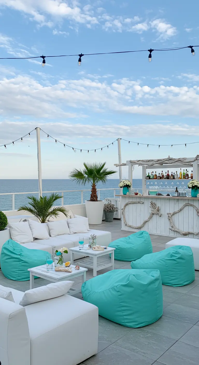 Rooftop bord de mer avec mobilier blanc, poufs turquoise, guirlandes lumineuses et vue sur l'océan.