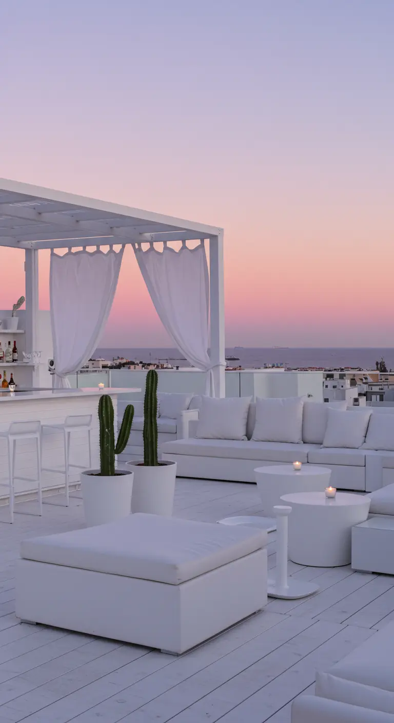 Rooftop lounge tout blanc avec une pergola, des voilages et des canapés confortables.