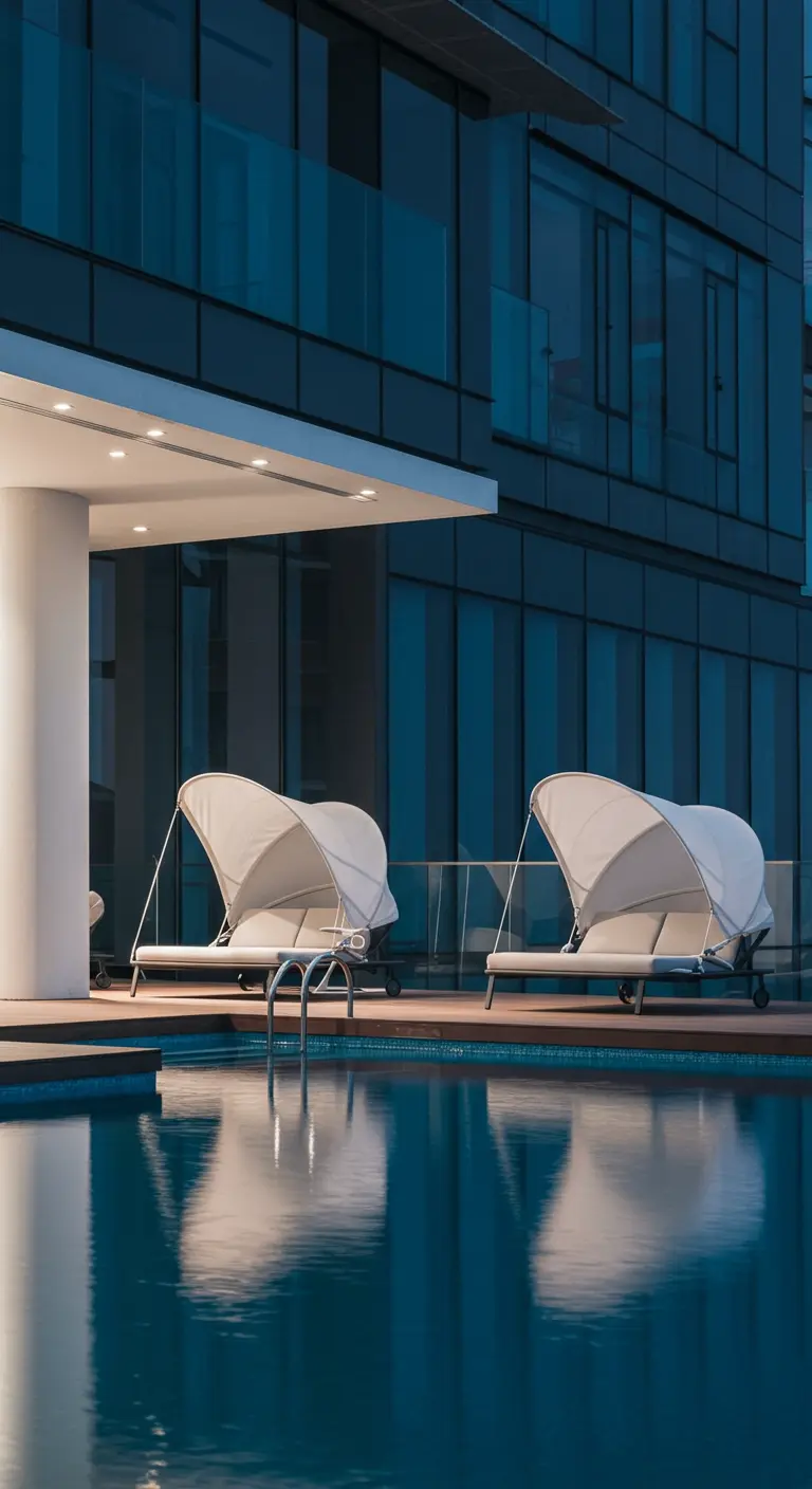Piscine au pied d'un immeuble moderne la nuit, avec deux transats à baldaquin aux lignes épurées.